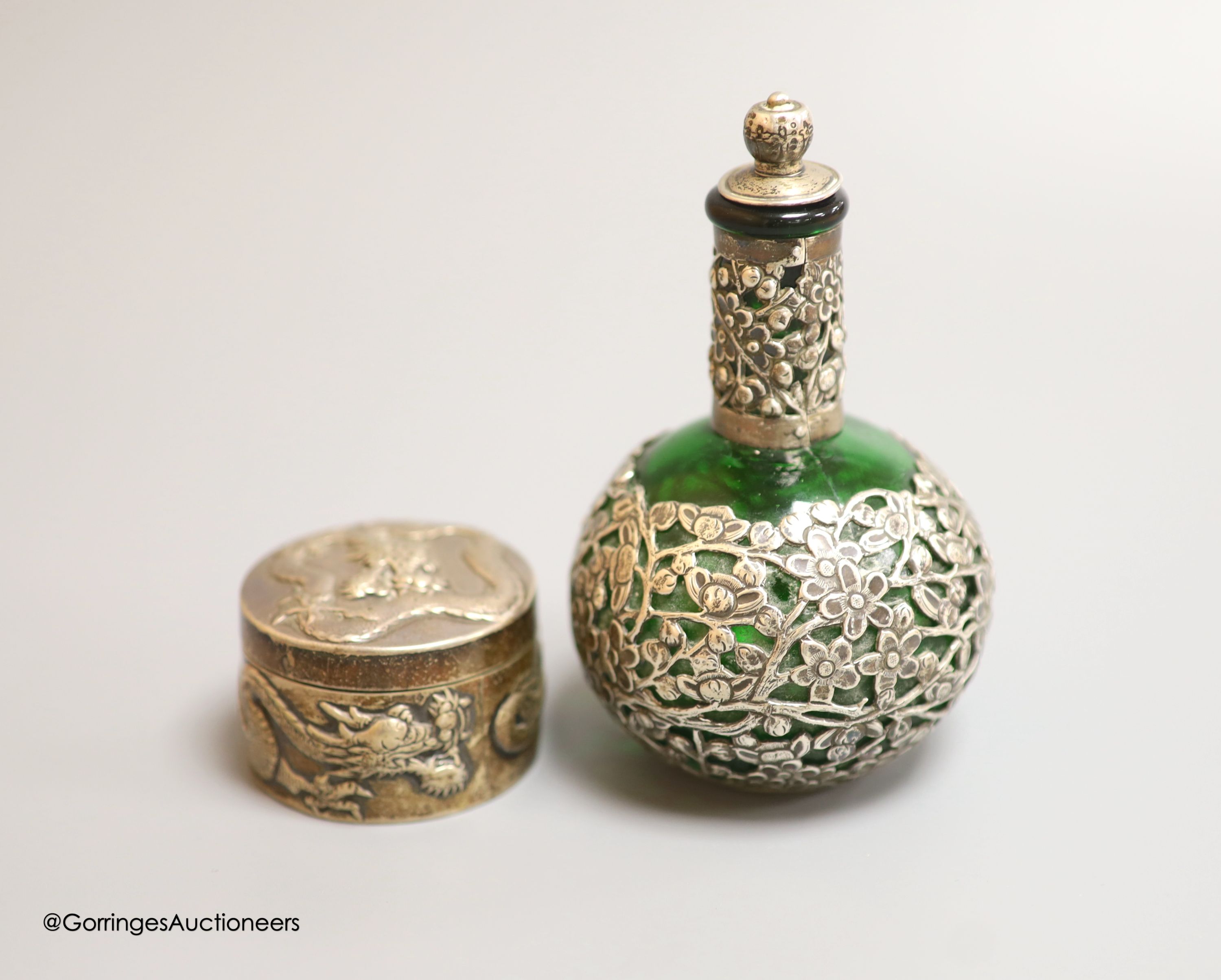 A late 19th/early 20th century Chinese Export white metal circular box, by Wang Hing, embossed with dragons, diameter 5cm, together with a similar white metal overlaid green glass scent flask by Wang Hing, height 11.6cm.